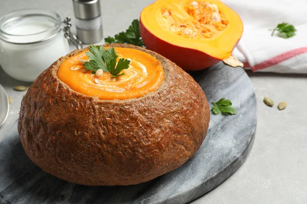 Tasty pumpkin cream soup in bread loaf on grey table — ストック写真