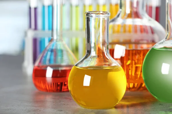 Флорентийская колба с разноцветной жидкостью на сером каменном столе в лаборатории — стоковое фото