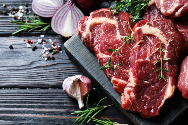 Bifes de carne crua frescos em mesa de madeira preta, flat lay — Fotografia de Stock