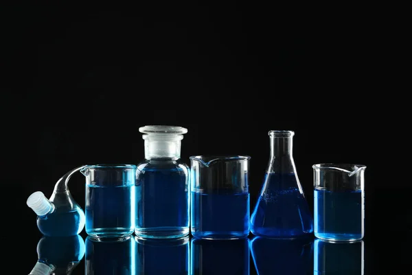 Vetreria da laboratorio con liquidi blu su fondo nero — Foto Stock