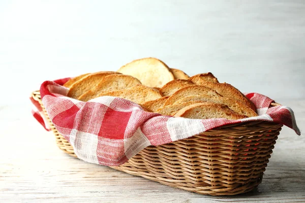 Fette di pane tostato in cesto su tavolo di legno bianco — Foto Stock