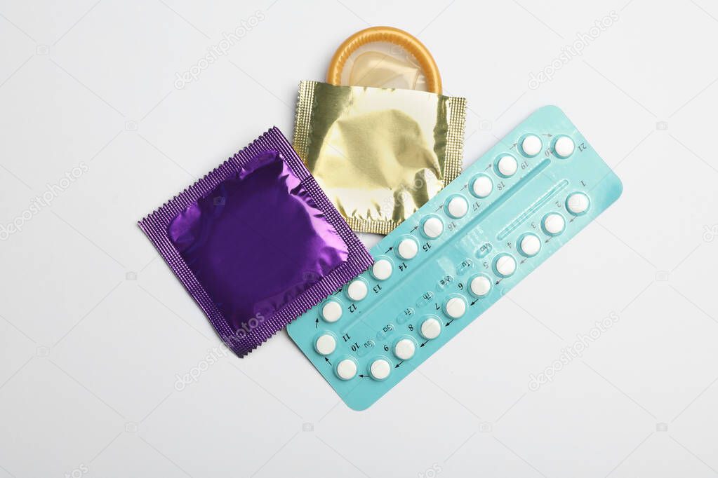 Condoms and birth control pills on light grey background, flat lay. Safe sex concept