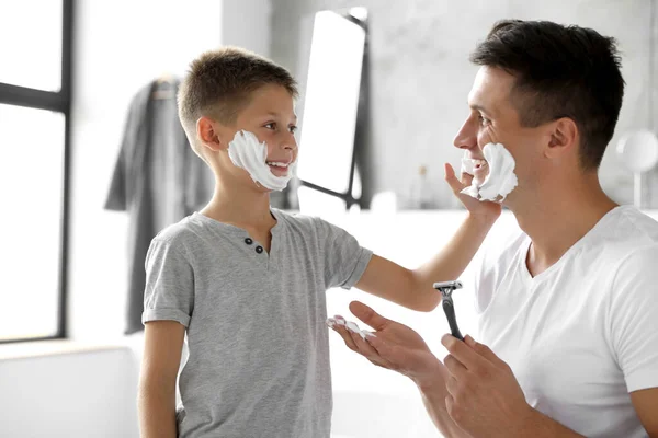 Son applying shaving foam onto father\'s face in bathroom