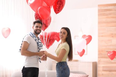 Oturma odasında kalp şeklinde balonları olan mutlu genç bir çift. Sevgililer Günü kutlaması