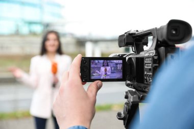 Şehir caddesinde çalışan genç erkek gazeteci ve video operatörü, kamera ekranına odaklanın