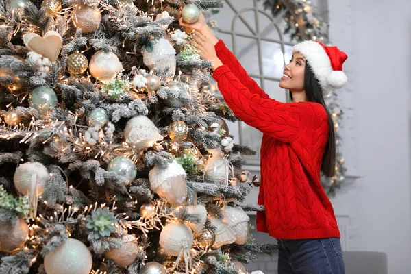 Šťastná mladá žena v santa klobouk zdobení vánoční stromeček doma — Stock fotografie