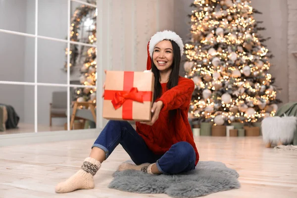Счастливая молодая женщина в шляпе Санта с рождественским подарком дома — стоковое фото