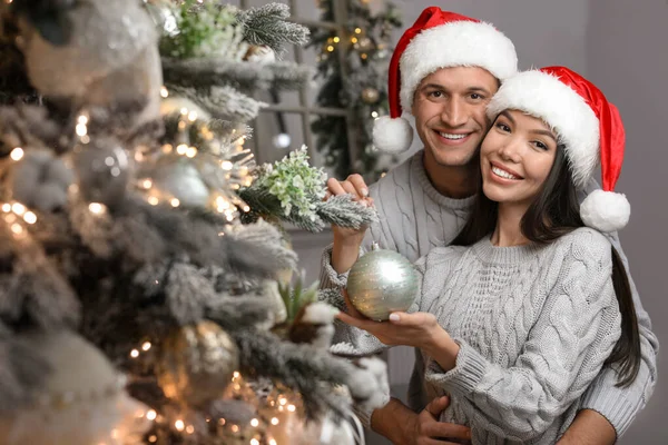 幸せな若いですカップルでサンタ帽子装飾クリスマスツリートータル — ストック写真
