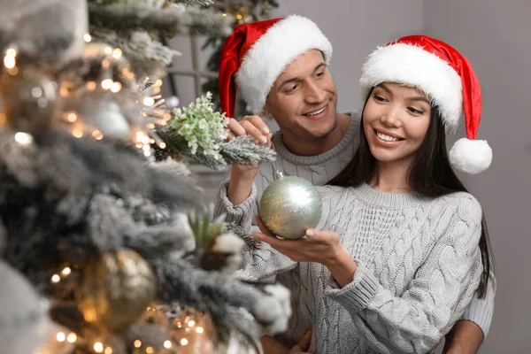 Happy young couple in Santa hats decorating Christmas tree toget — Stock Photo, Image