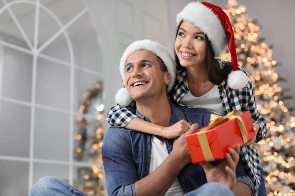 幸せな若いカップルでサンタの帽子とともにクリスマスプレゼントに家 — ストック写真