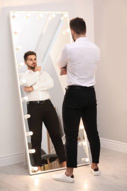Genç adam, evinde büyük bir aynada kendine bakıyor.