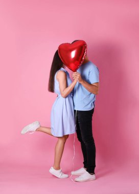 Pembe arka planda kalp şeklinde bir balonun arkasına saklanan sevimli bir çift. Sevgililer Günü kutlaması