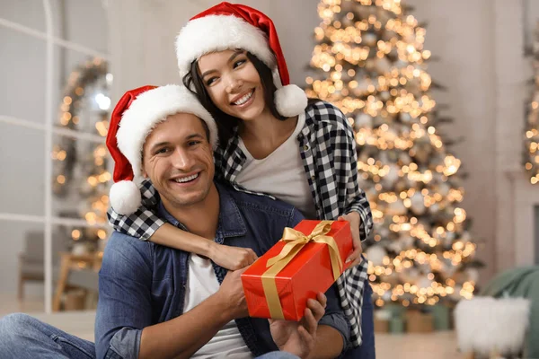 Šťastný mladý pár v Santa klobouky s vánoční dárek doma — Stock fotografie