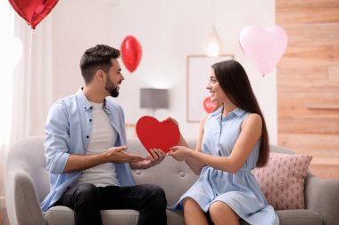 Oturma odasında kalp şeklinde balonlarla süslenmiş sevimli bir çift. Sevgililer Günü kutlaması