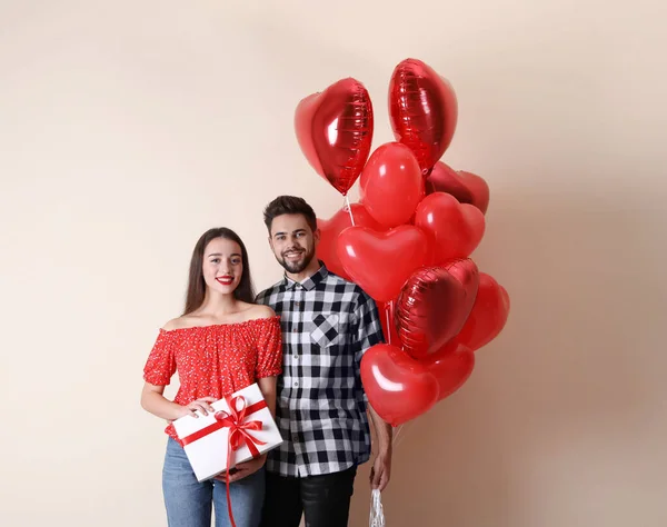 Szczęśliwa Młoda Para Pudełkiem Prezentów Balonami Kształcie Serca Beżowym Tle — Zdjęcie stockowe
