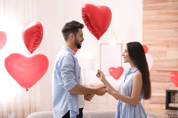 Happy young couple in living room decorated with heart shaped balloons. Valentine\'s day celebration