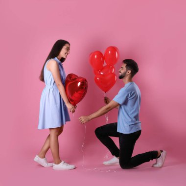 Pembe arka planda kalp şeklinde balonları olan sevimli bir çift. Sevgililer Günü kutlaması