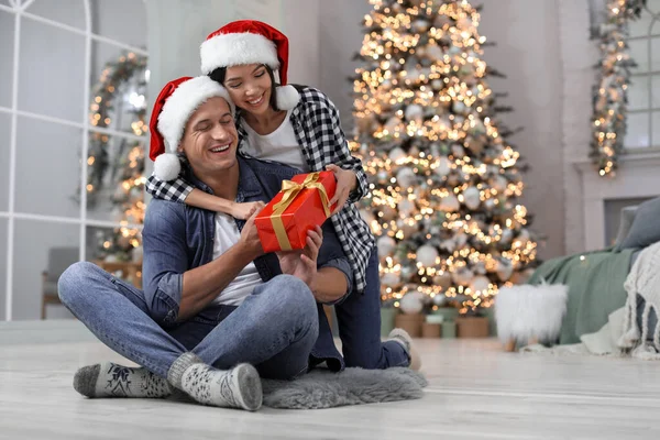 幸せな若いカップルでサンタの帽子とともにクリスマスプレゼントに家 — ストック写真