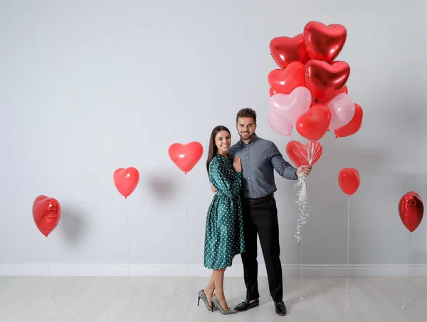 Szczęśliwa Młoda Para Balonami Kształcie Serca Pobliżu Ściany Światła Walentynki — Zdjęcie stockowe