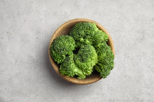 Fresh green broccoli in bowl on light table, top view