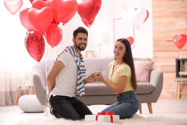Oturma odasında kalp şeklinde balonları olan mutlu genç bir çift. Sevgililer Günü kutlaması