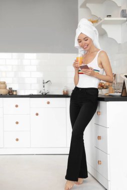 Havlu, telefon ve mutfakta bir bardak meyve suyu olan güzel bir kadın.