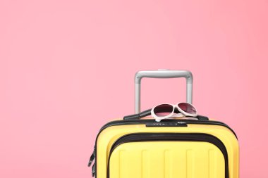 Pembe arka planda güneş gözlüklü sarı bavul. Te için boşluk