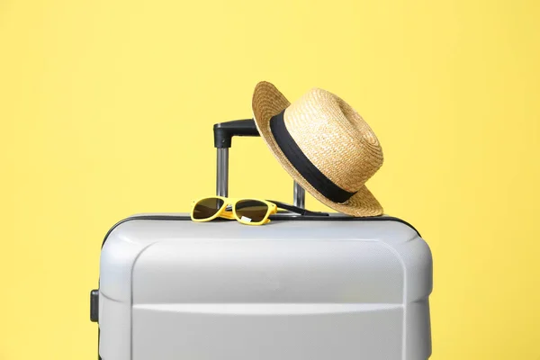 Valigia grigia con occhiali da sole e cappello su sfondo giallo — Foto Stock