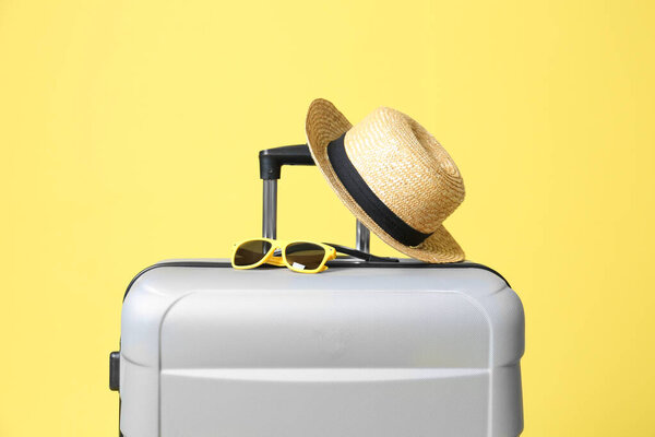 Grey suitcase with sunglasses and hat on yellow background