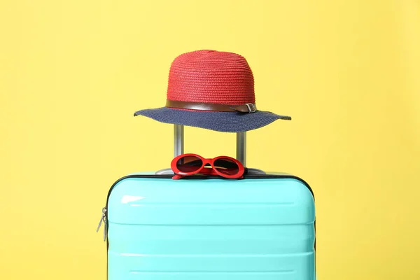 Valigia turchese con occhiali da sole e cappello su sfondo giallo — Foto Stock