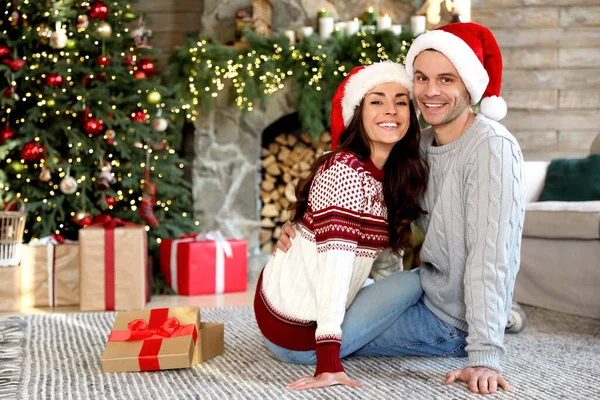 幸せな若いカップル身に着けているサンタの帽子でリビングルーム装飾されたクリスマス — ストック写真