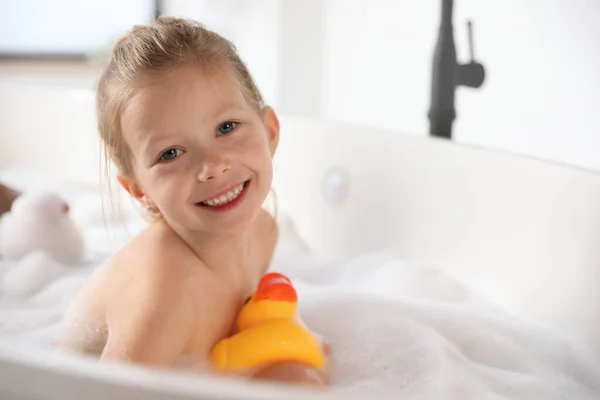 Cute little girl taking bubble bath at home