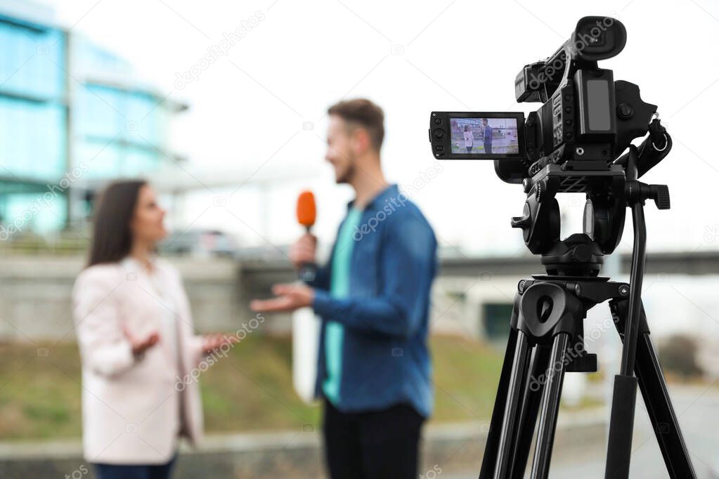 Young journalist interviewing businesswoman on city street, focus on camera display