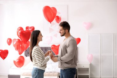 Yatak odasında kalp şeklinde balonlarla süslenmiş genç bir çift. Sevgililer Günü kutlaması