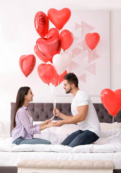 Romantic couple with heart shaped balloons in bedroom. Valentine\'s day celebration