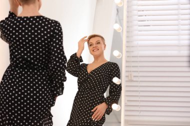 Güzel, olgun bir kadın büyük aynada kendine bakıyor.