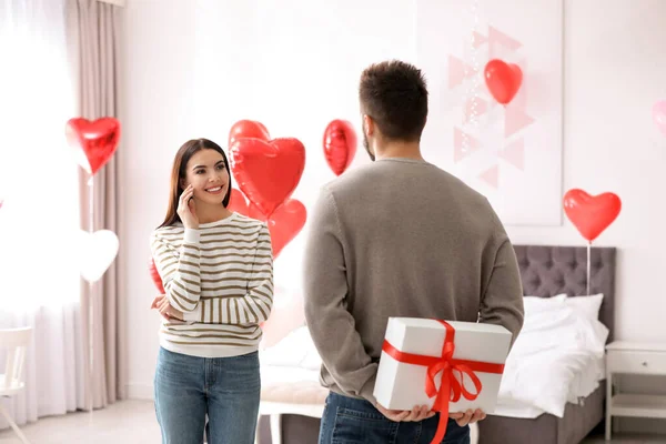 在卧室里送给女朋友礼物的年轻人用心形气球装饰着 情人节庆祝活动 — 图库照片