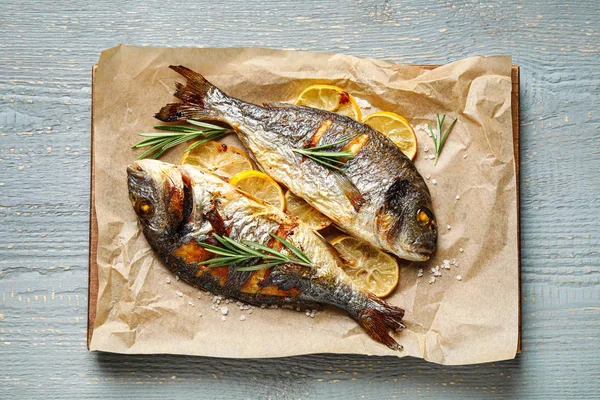 Delicious roasted fish with lemon on grey wooden table, top view