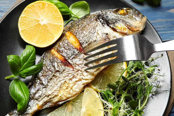 Delicious roasted fish with lemon and greens on plate, closeup