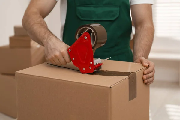 Man packing box with adhesive tape indoors, closeup. Moving serv — Stock Photo, Image