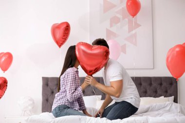 Yatak odasında kalp şeklinde bir balonun arkasına saklanan romantik bir çift. Sevgililer Günü kutlaması