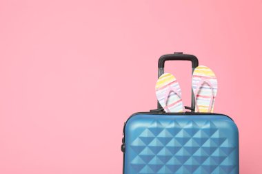 Pembe arka planda parmak arası terlikleri olan şık mavi bir bavul. Boşluk 