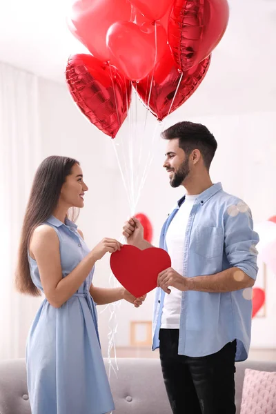 Lovely couple with heart shaped balloons in living room. Valentine\'s day celebration