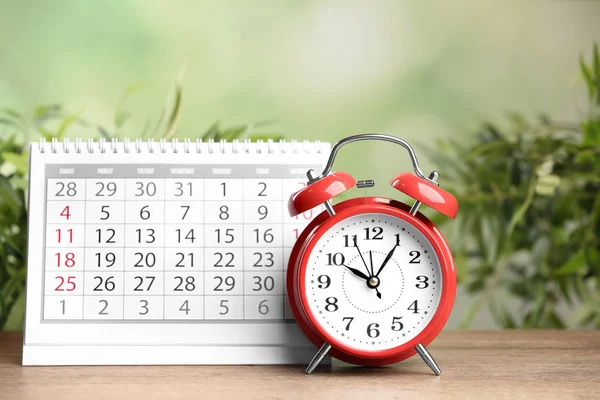木制桌子上的日历和闹钟 在模糊的绿色背景下 — 图库照片