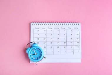 Pembe zemin üzerinde takvim ve alarm saati düz yatıyordu