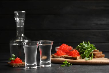 Soğuk Rus votkası ve siyah masada kırmızı havyarlı sandviçler.