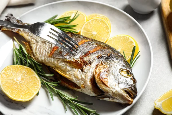 Delicious roasted fish with lemon on grey table, closeup