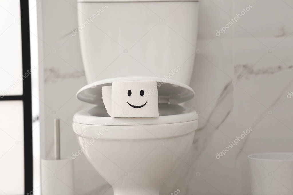 Roll of paper with funny face on toilet bowl in bathroom