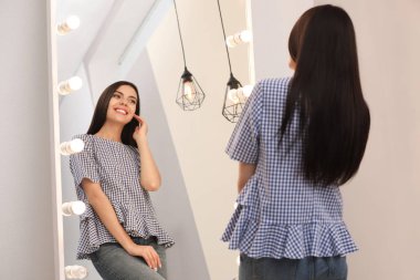 Genç ve çekici bir kadın evinde kendine şık bir aynada bakıyor.