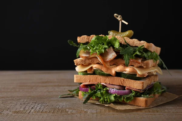 Tasty sandwich with chicken, ham and bacon on wooden table against black background. Space for text